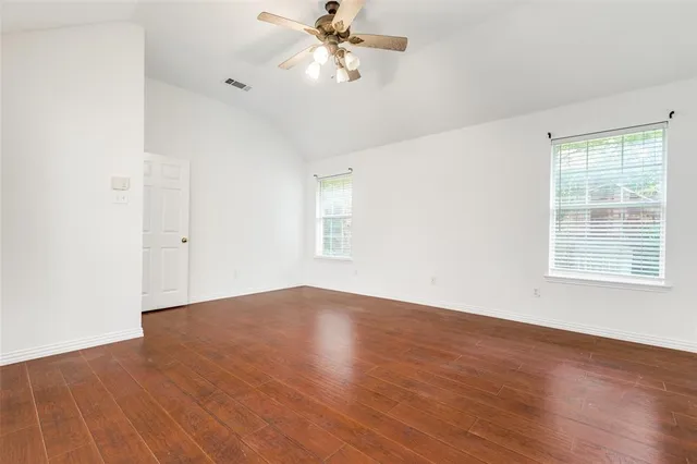 an empty room with wooden floor fan and windows