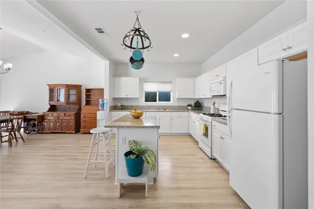 a kitchen with stainless steel appliances a refrigerator a stove top oven a sink dishwasher and white cabinets with wooden floor