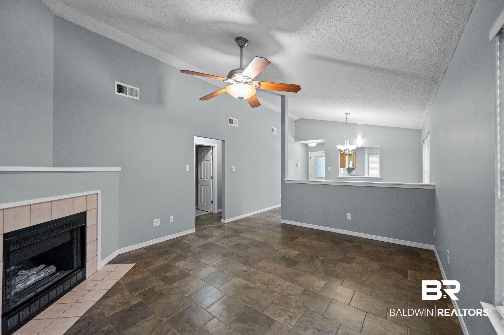 3744 Pepper Ridge Drive Mobile, AL 36693 - Photo 7 of 29 Unfurnished living room with a tiled fireplace, a textured ceiling, a chandelier, stone finish flooring, and a ceiling fan