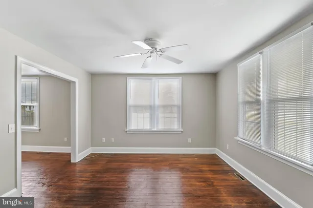 an empty room with wooden floor chandelier fan and windows