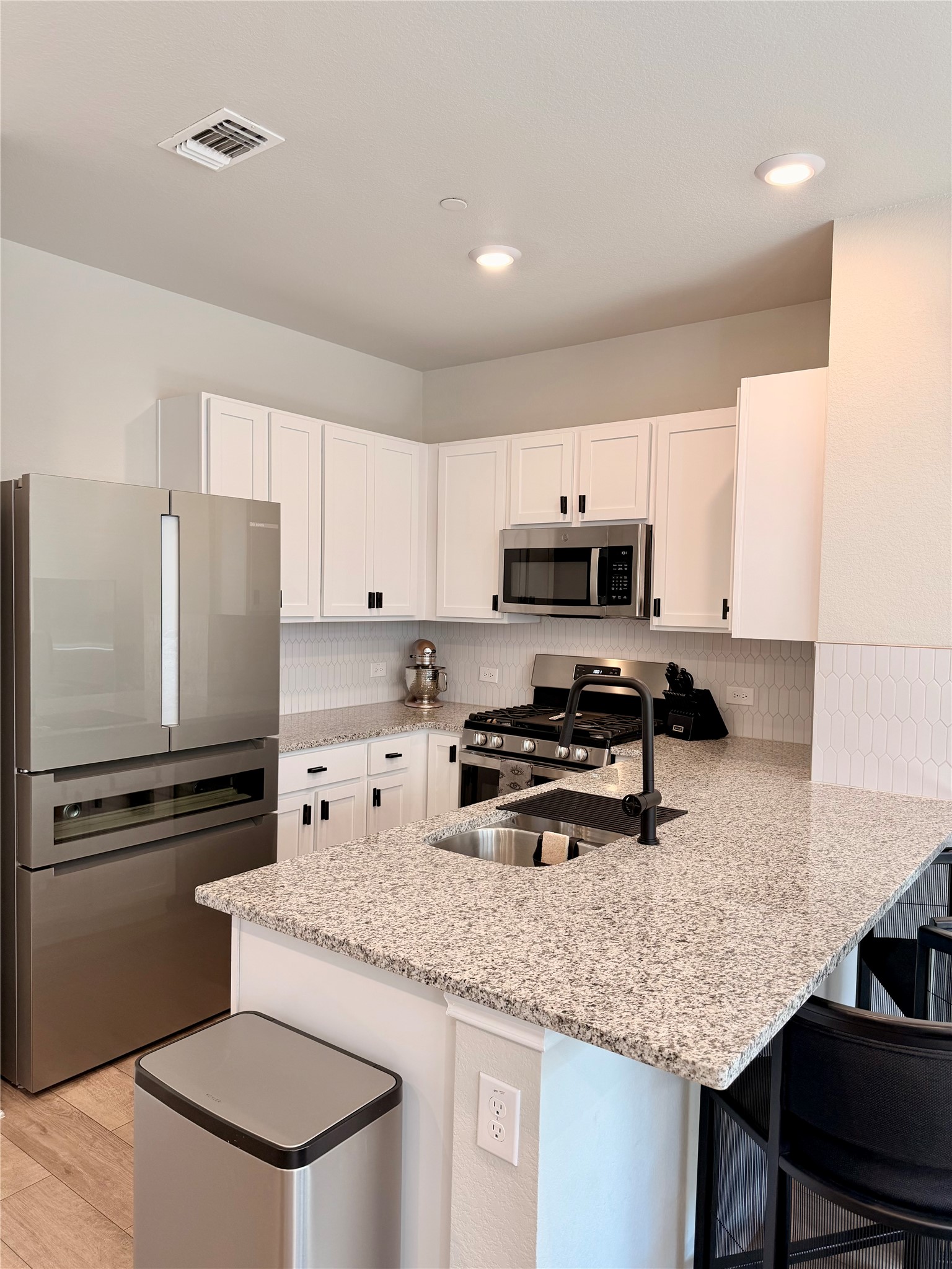 9015 Cattle Baron Path, Unit 1803 Austin, TX 78747 - Photo 5 of 23 Kitchen w/ backsplash, white cabinets, stainless steel appliances, a breakfast bar, black cabinet pulls, and light stone countertops