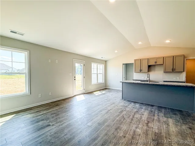 a large kitchen with stainless steel appliances granite countertop a large counter top a wooden floors and a large window