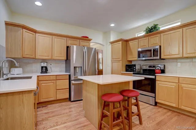 a kitchen with granite countertop wooden cabinets a stove a sink dishwasher and a refrigerator with wooden floor