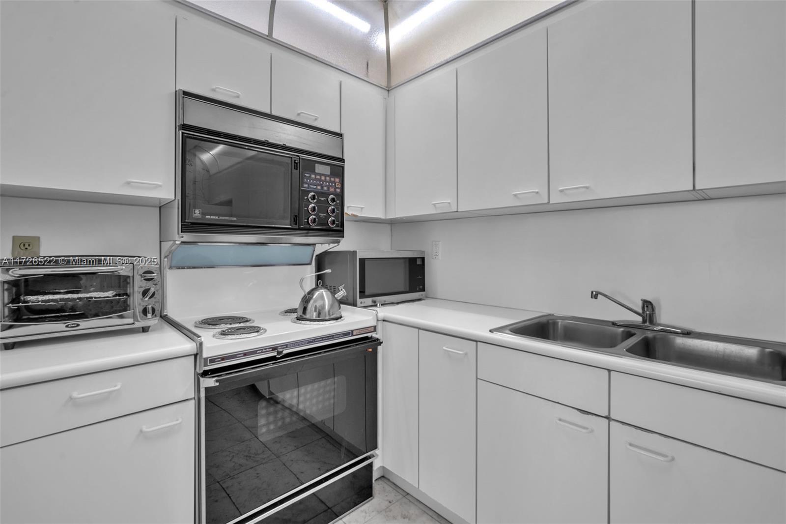 9341 Collins Avenue, Unit 1205 Surfside, FL 33154 - Photo 16 of 29 a kitchen with white cabinets appliances and sink
