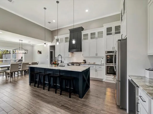 a large kitchen with stainless steel appliances kitchen island granite countertop a large stove a refrigerator a sink a dining table and chairs with wooden floor