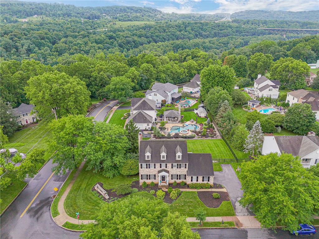 An aerial perspective showcases a classic brick home nestled within a lush, forested valley.