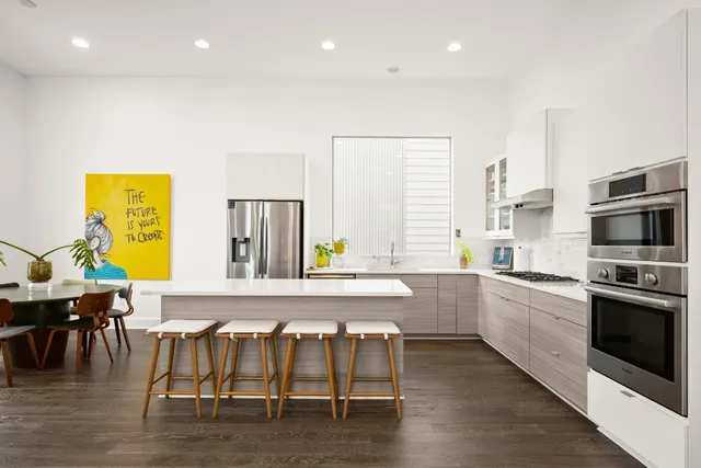 a kitchen with stainless steel appliances granite countertop a stove top oven a sink a dining table and chairs with wooden floor