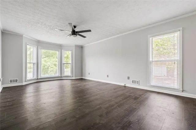 an empty room with wooden floor chandelier fan and windows