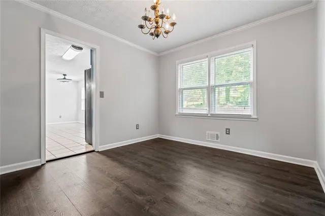 an empty room with wooden floor chandelier and windows