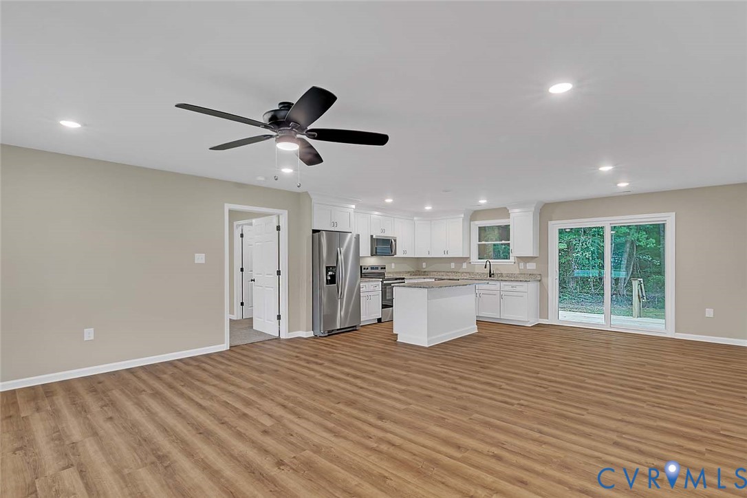 5008 Chestnut Fork Road Gloucester, VA 23061 - Photo 5 of 35 a open kitchen with white cabinets a sink dishwasher a dining table and chairs with wooden floor