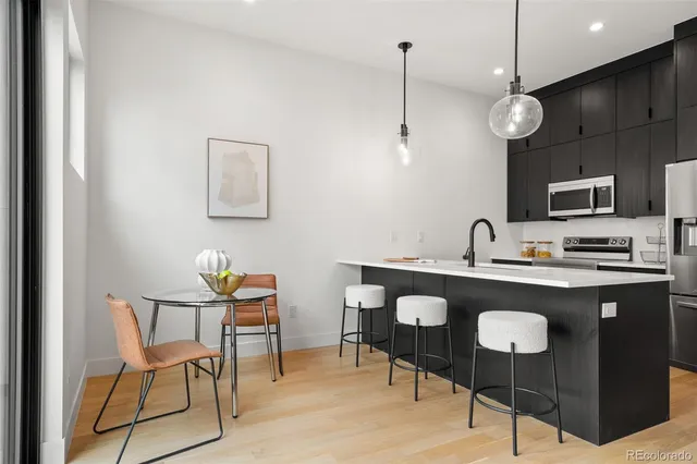 a kitchen with stainless steel appliances granite countertop a sink a stove a refrigerator a dining table with white cabinets and chairs