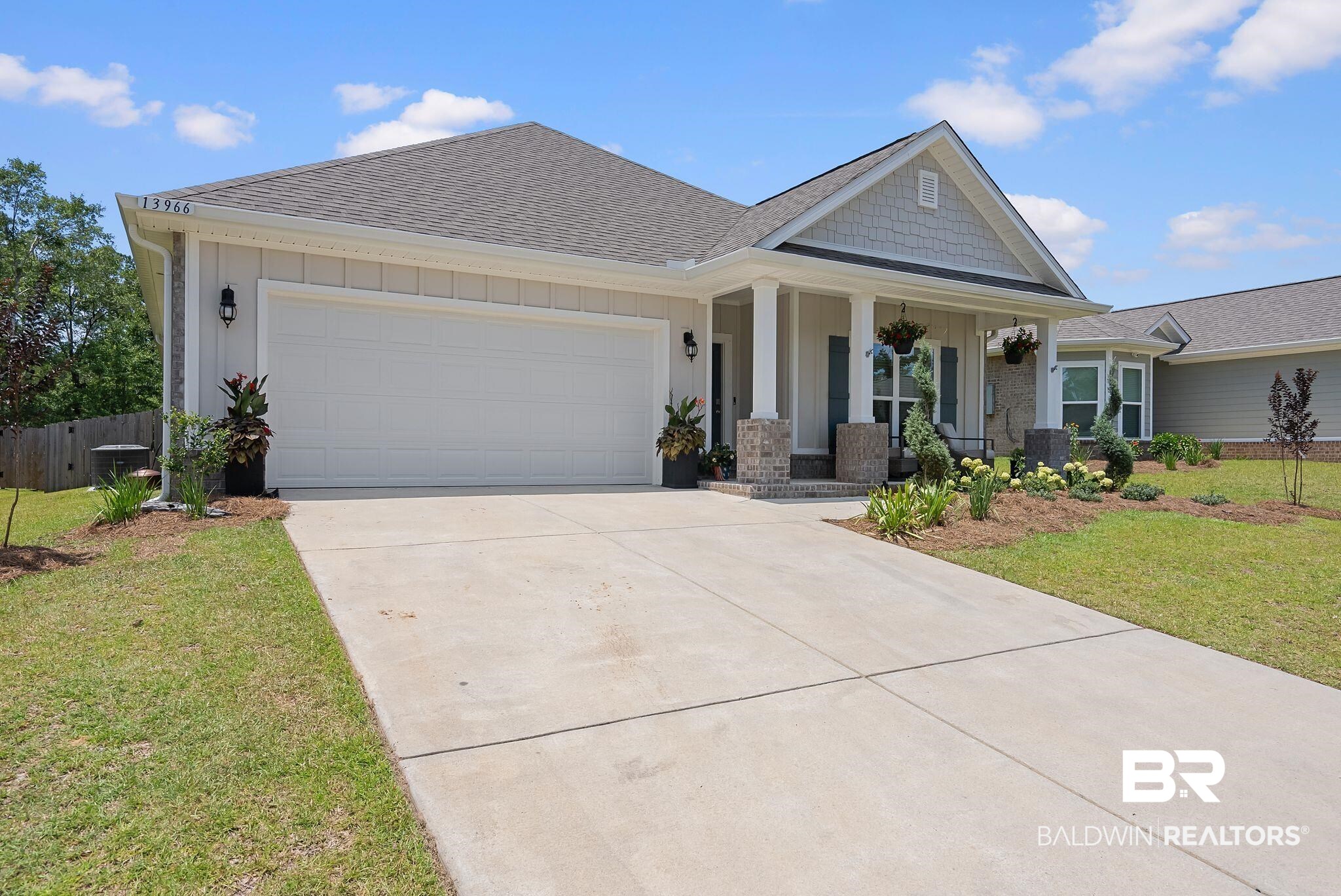 13966 Antler Hl Road Daphne, AL 36527 - Photo 31 of 44 Single-story residence featuring light-colored siding, a covered entry with stone-accented pillars, a gray shingle roof, a two-car garage, and a landscaped front yard