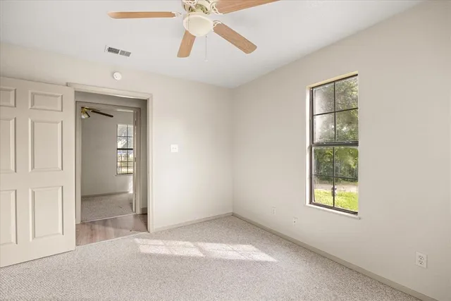 an empty room with chandelier fan and windows