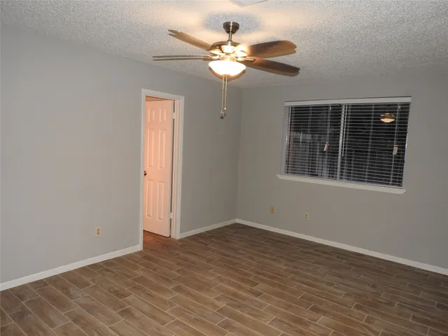 an empty room with wooden floor chandelier fan and windows