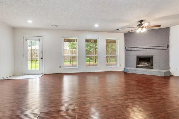 an empty room with wooden floor fireplace and windows