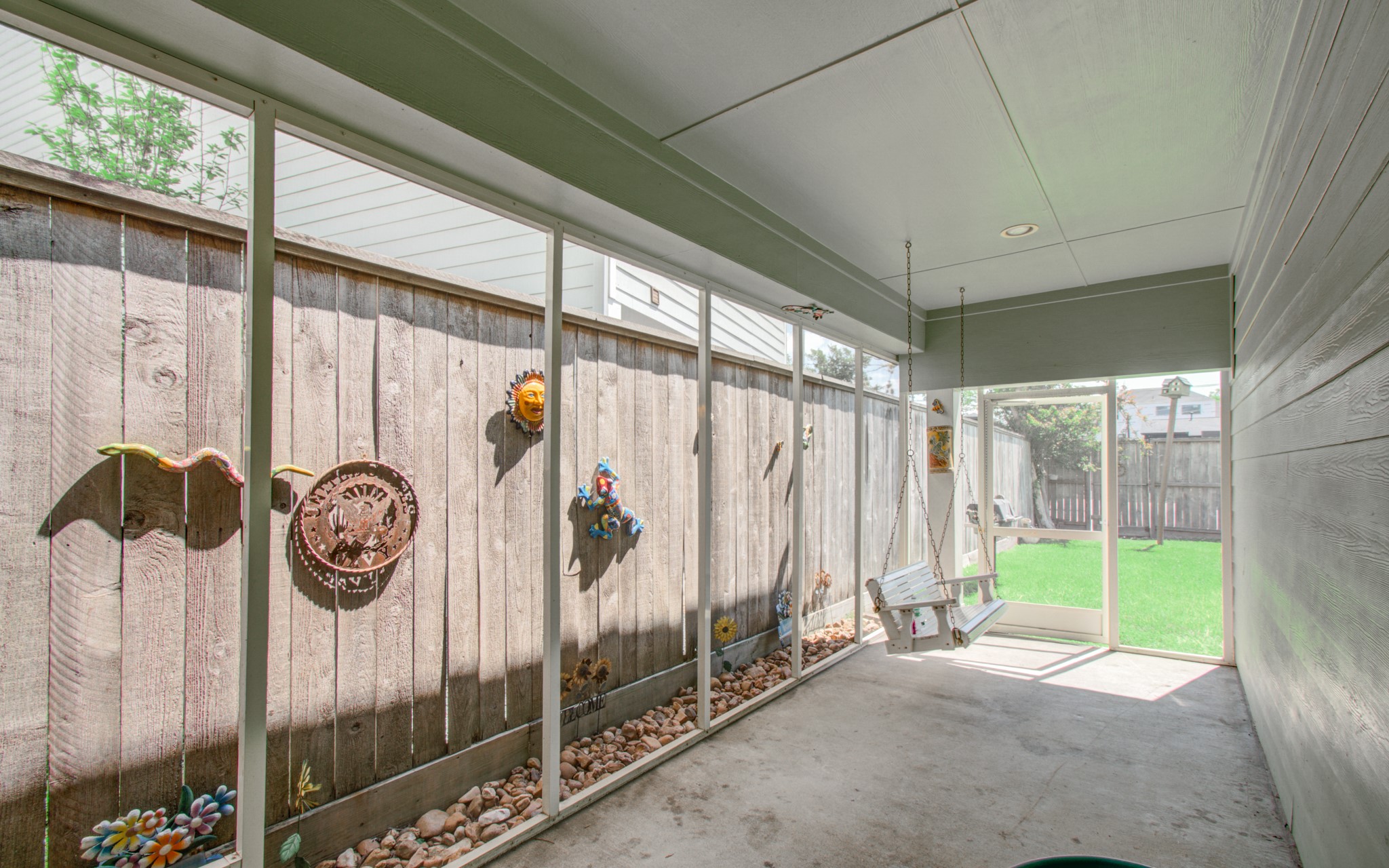 6621 North Main Street Houston, TX 77009 - Photo 31 of 41 This photo shows a bright, enclosed patio with screened walls adorned with decorative art pieces. There's a cozy swing seat, and it opens up to a backyard with a well-maintained lawn, perfect for relaxation or entertaining.