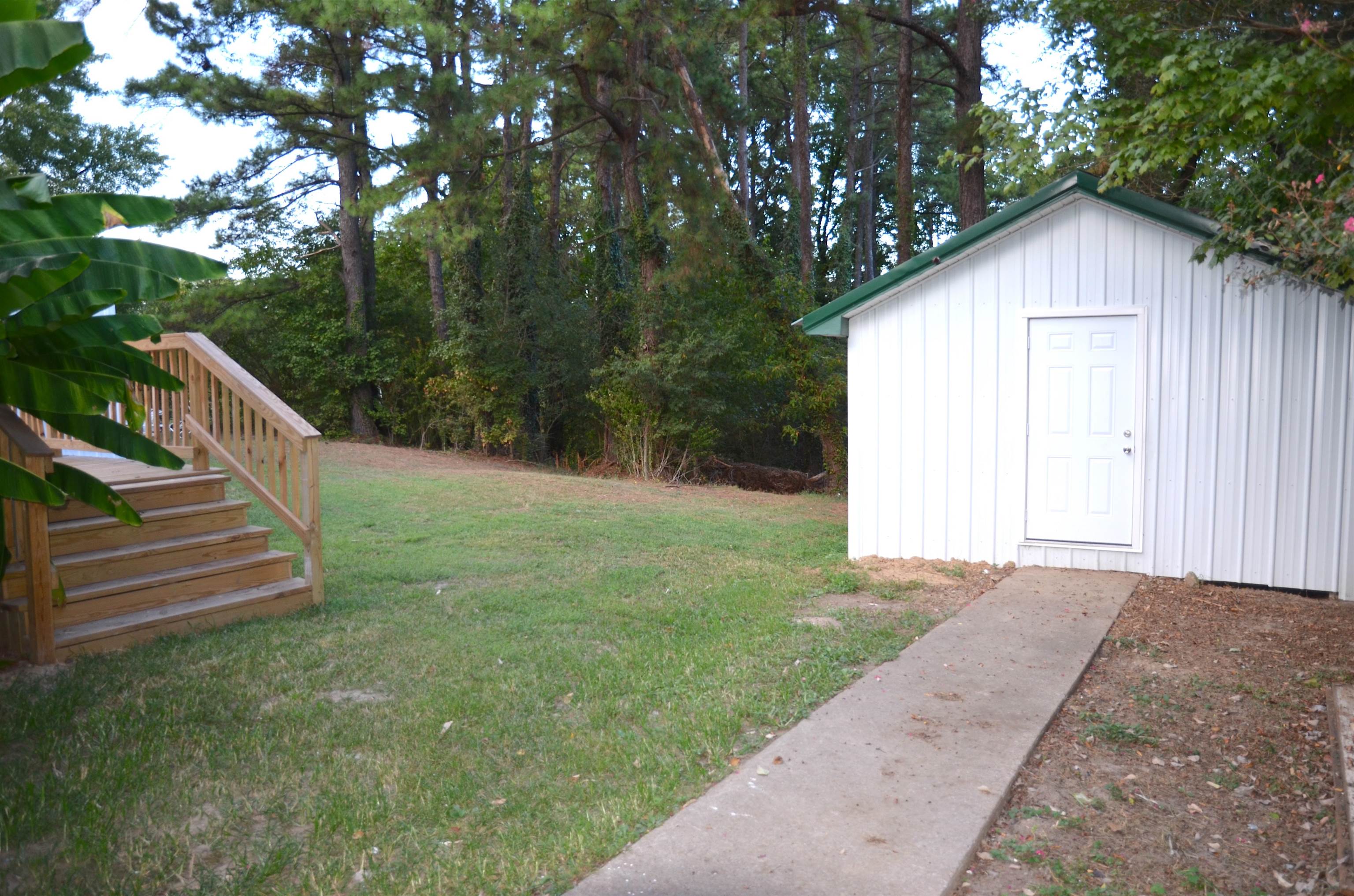2464 Edith-Nankipoo Road Ripley, TN 38063 - Photo 21 of 22 Expansive grassy yard with a wood deck and stairs, a separate storage building with a green roof, and a concrete pathway