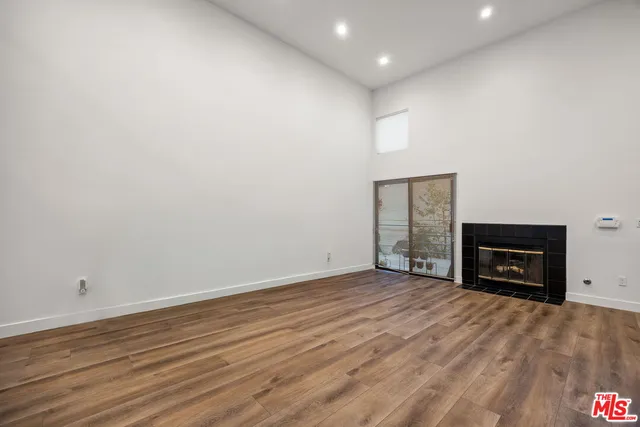 a view of an empty room with wooden floor fireplace and a window
