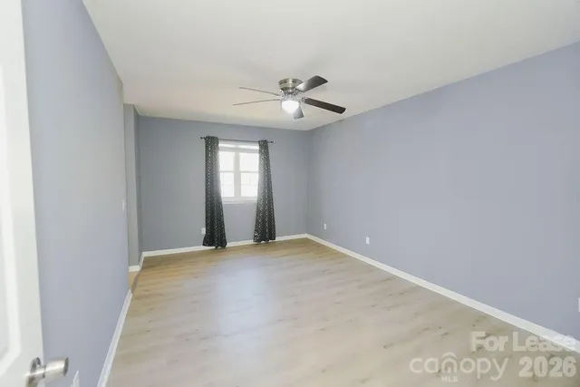 an empty room with chandelier fan and windows