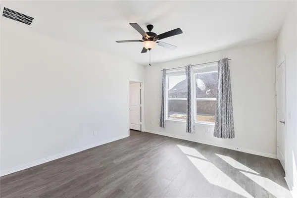 an empty room with wooden floor fan and windows