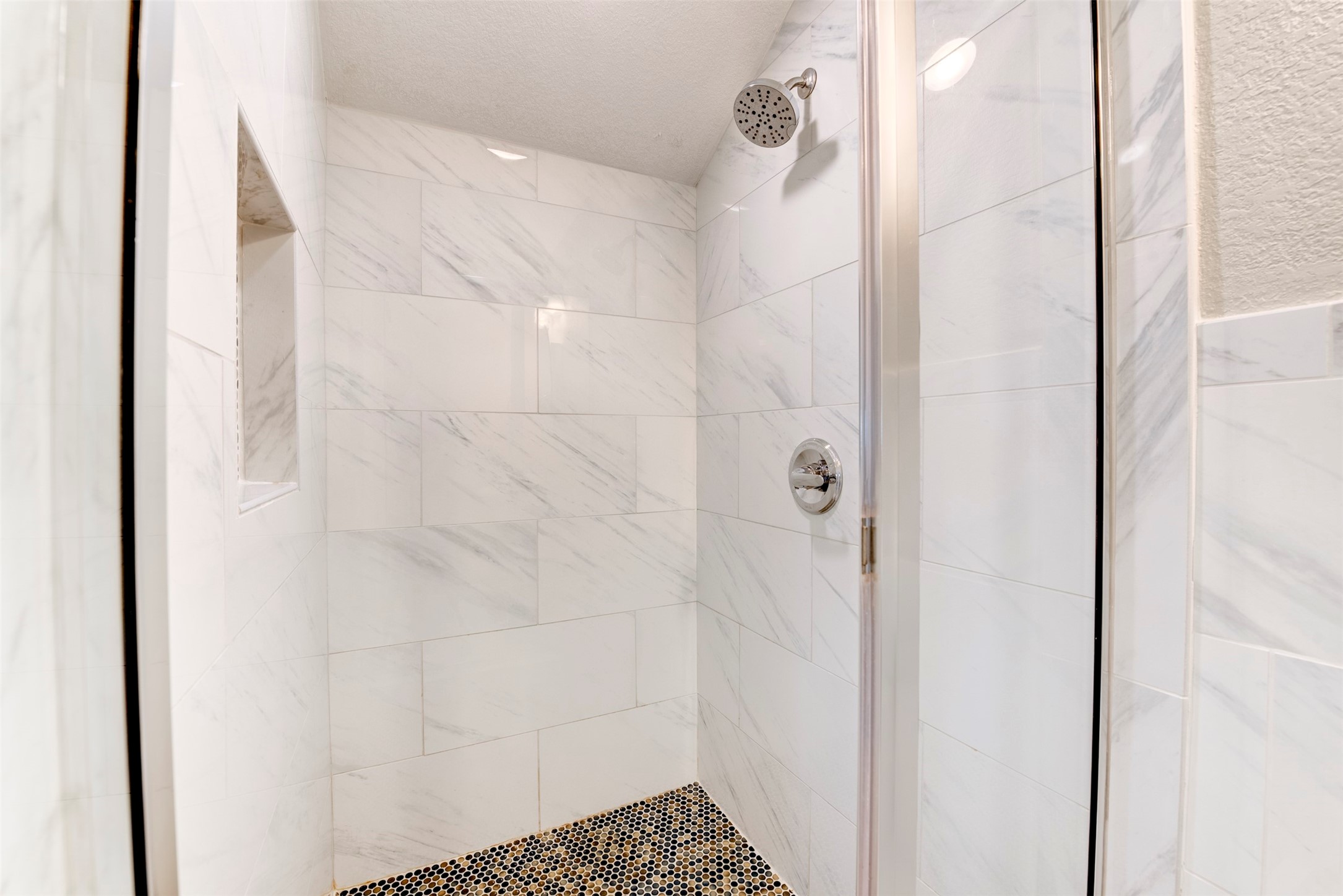 109 Dresden Street Houston, TX 77012 - Photo 29 of 43 This photo shows a modern, spacious shower with elegant white marble tile walls and a sleek glass door. There's a built-in niche for storage and a stylish showerhead, creating a luxurious bathroom experience.