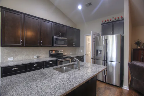 a kitchen with stainless steel appliances granite countertop a refrigerator a stove and a sink with wooden cabinets