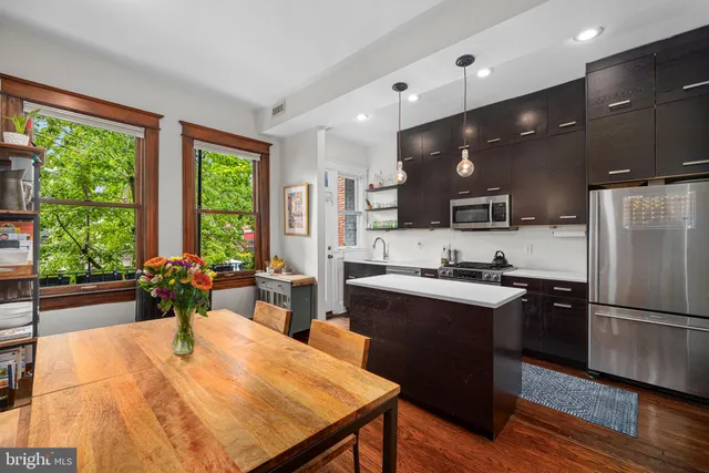 a kitchen with stainless steel appliances kitchen island granite countertop a stove a refrigerator a sink a dining table and chairs with wooden floor