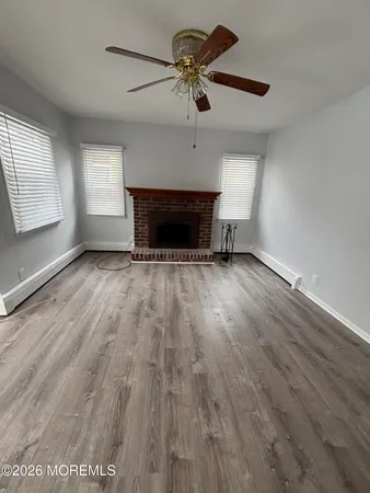 an empty room with wooden floor a ceiling fan a fireplace and windows