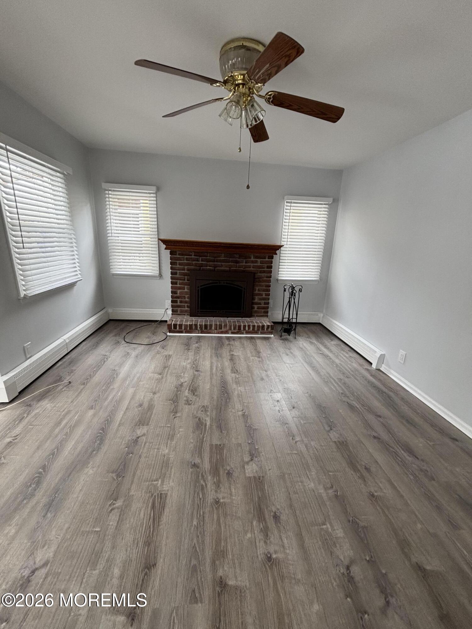 507 Riverside Drive South Brick, NJ 08723 - Photo 10 of 17 an empty room with wooden floor a ceiling fan a fireplace and windows