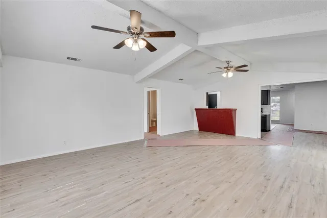 a view of an empty room with wooden floor and a ceiling fan