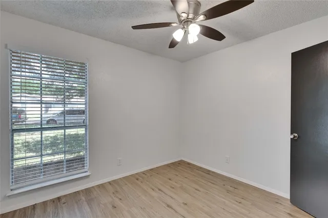 an empty room with wooden floor fan and windows