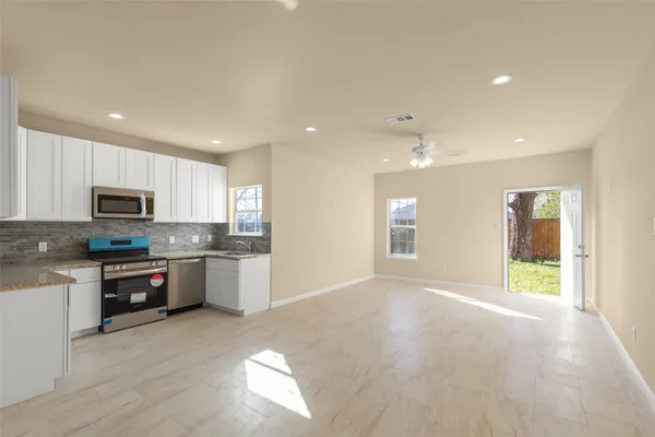 a open kitchen with stainless steel appliances granite countertop a stove top oven a sink dishwasher a refrigerator and white cabinets with wooden floor