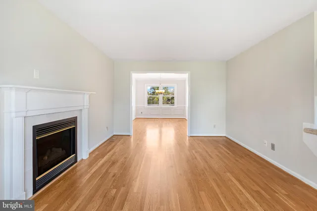 a view of an empty room with wooden floor fireplace and a window