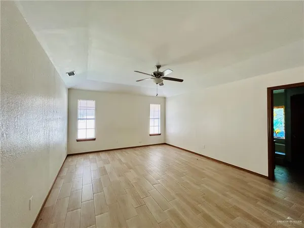 an empty room with wooden floor chandelier fan and windows