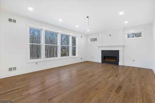 a view of an empty room with wooden floor fireplace and a window