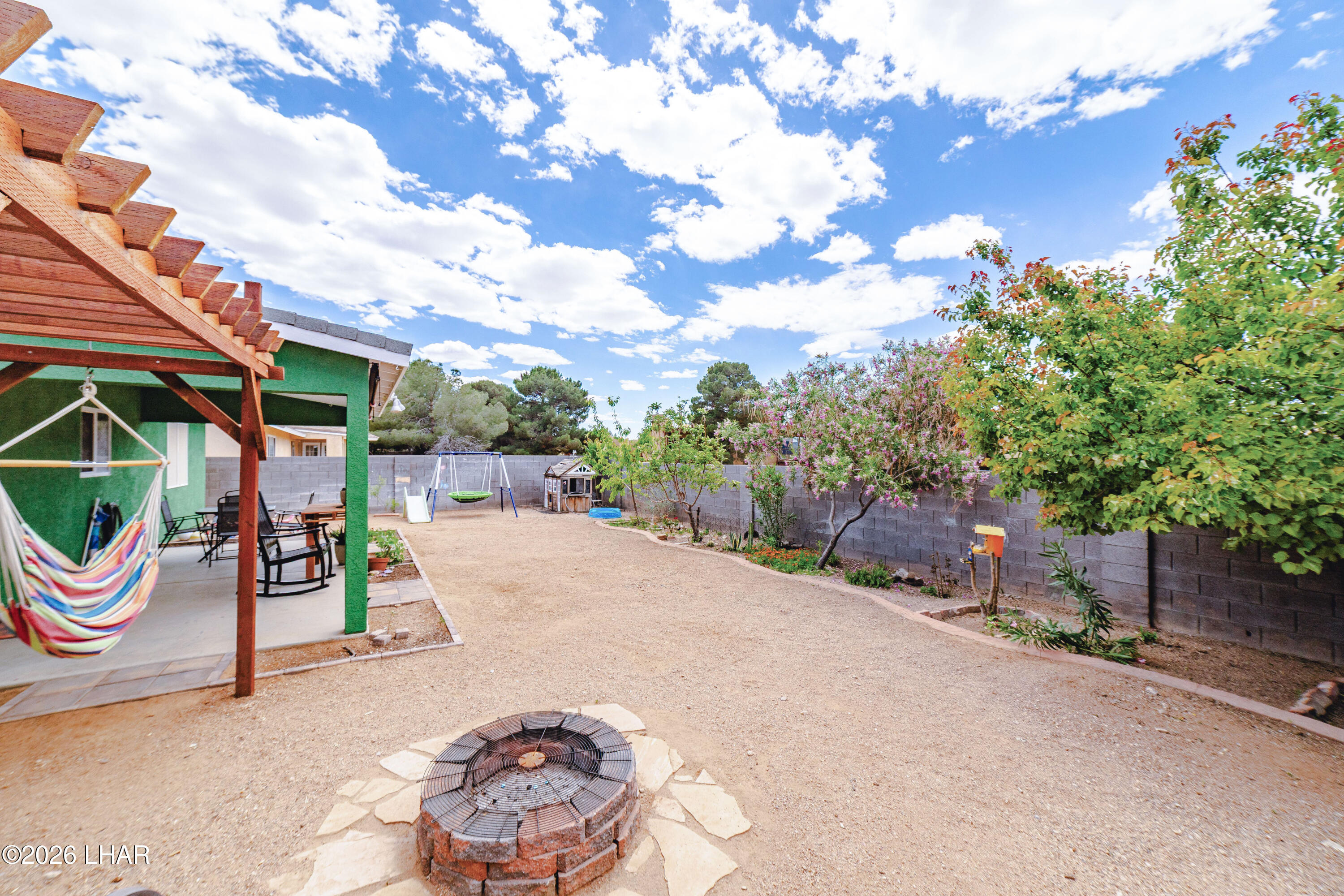 2177 Ridgeview Road Kingman, AZ 86401 - Photo 26 of 43 Expansive backyard featuring a stone fire pit, covered patio with wood pergola, mature trees, and privacy block wall fencing