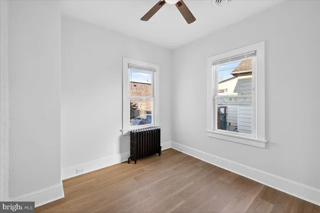 an empty room with chandelier fan and windows