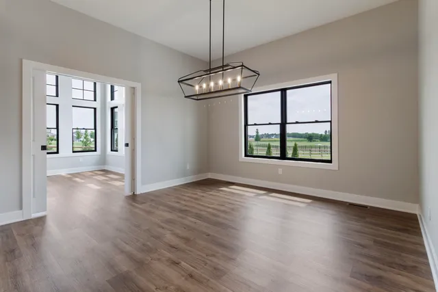 an empty room with wooden floor chandelier and windows