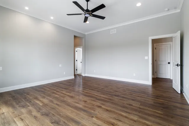 a view of an empty room with wooden floor and a ceiling fan