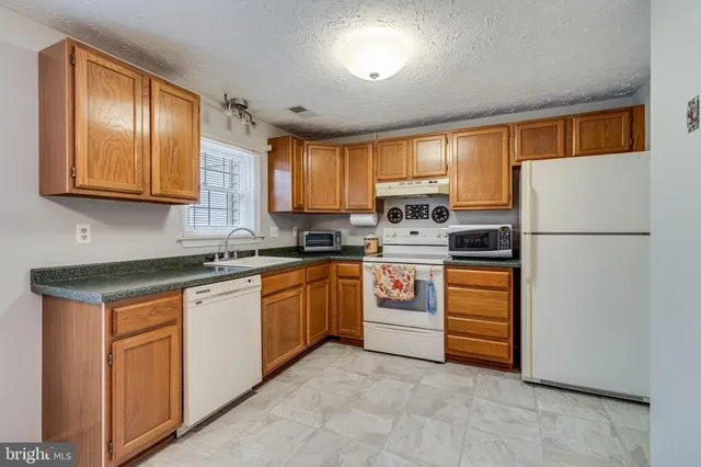 a kitchen with granite countertop a refrigerator a sink and white cabinets