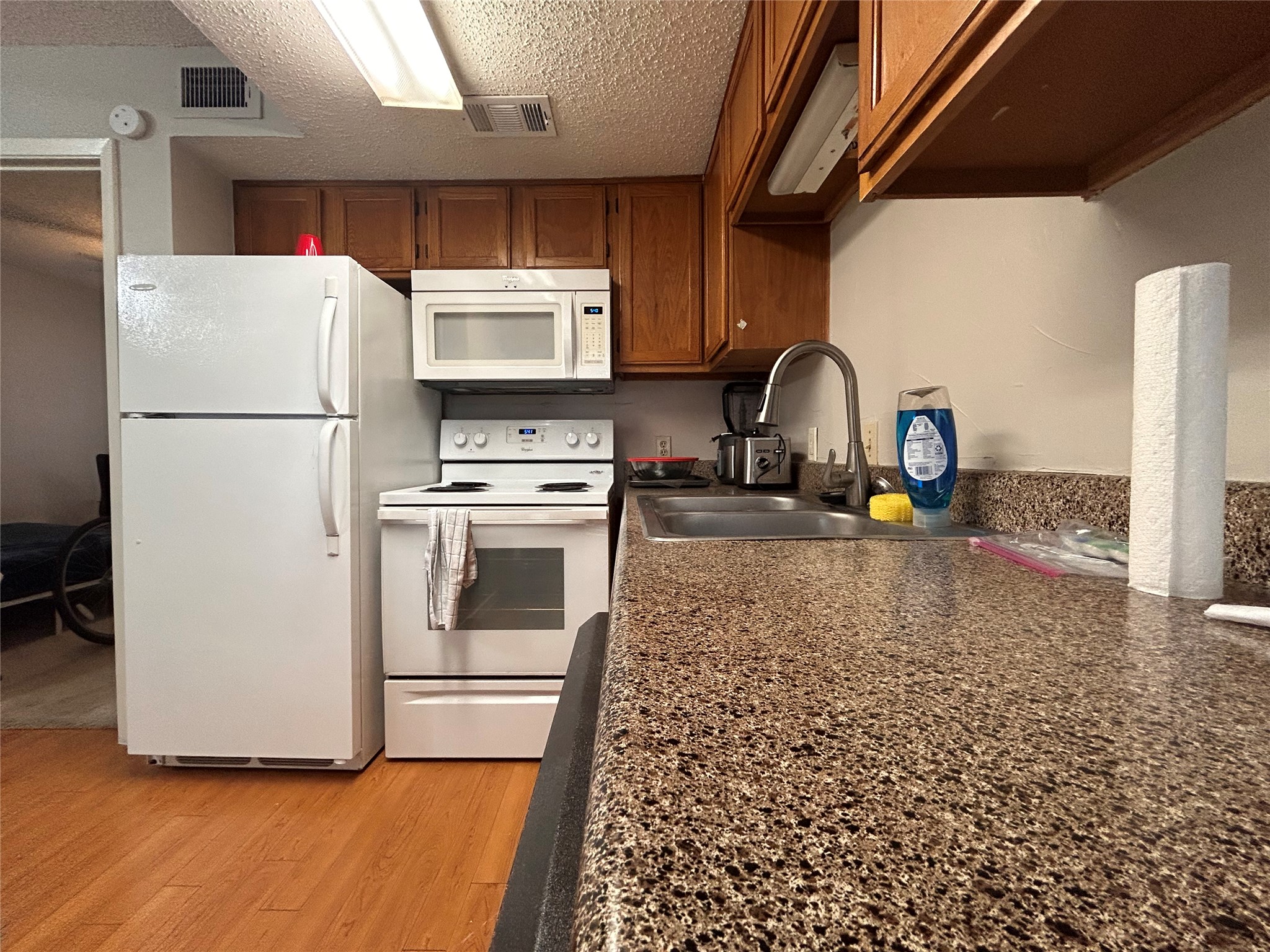 3115 Helms Street, Unit 109 Austin, TX 78705 - Photo 3 of 9 Kitchen with white appliances, light wood-type flooring, a textured ceiling, and wood finish cabinets