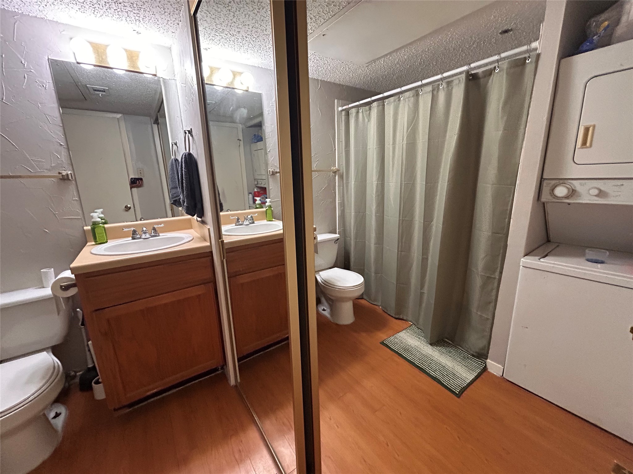 3115 Helms Street, Unit 109 Austin, TX 78705 - Photo 7 of 9 Bathroom with curtained shower, a textured wall, vanity, light wood-style floors, and stacked washer and dryer