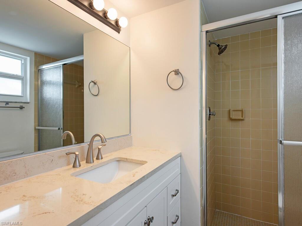 180 Turtle Lake Court, Unit 101 Naples, FL 34105 - Photo 6 of 10 a bathroom with a granite countertop sink a shower and a mirror