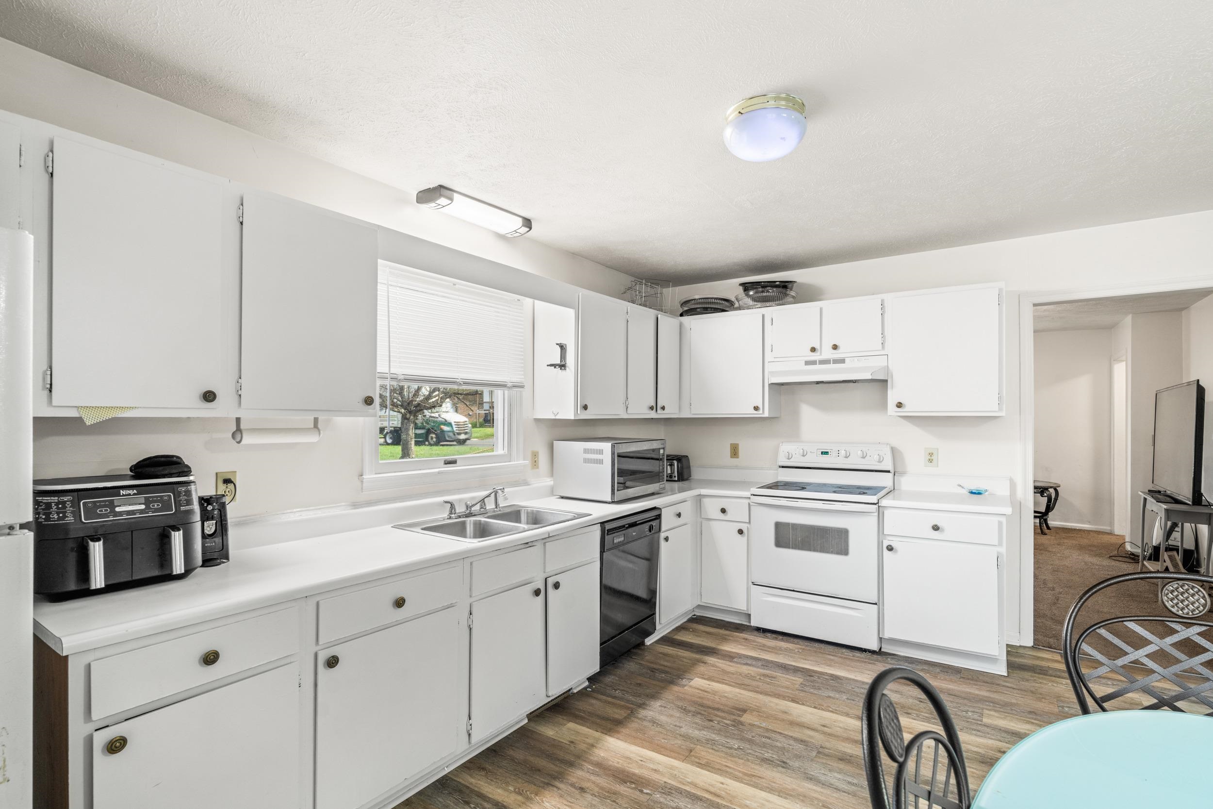 1316 East Main Street Waynesboro, VA 22980 - Photo 16 of 34 a kitchen with white cabinets a sink dishwasher and a stove with wooden floor