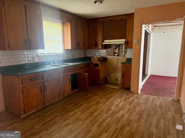 a kitchen with stainless steel appliances granite countertop a refrigerator a sink dishwasher a stove and white countertops with wooden floor