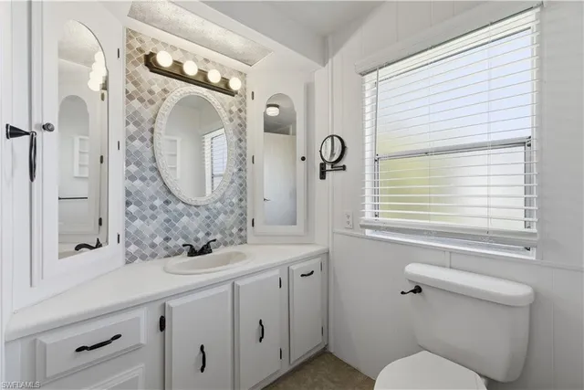 a bathroom with a granite countertop sink mirror toilet and next to a window