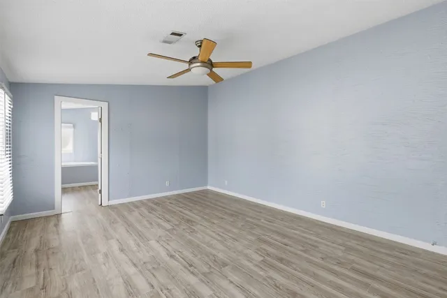 an empty room with wooden floor fan and windows