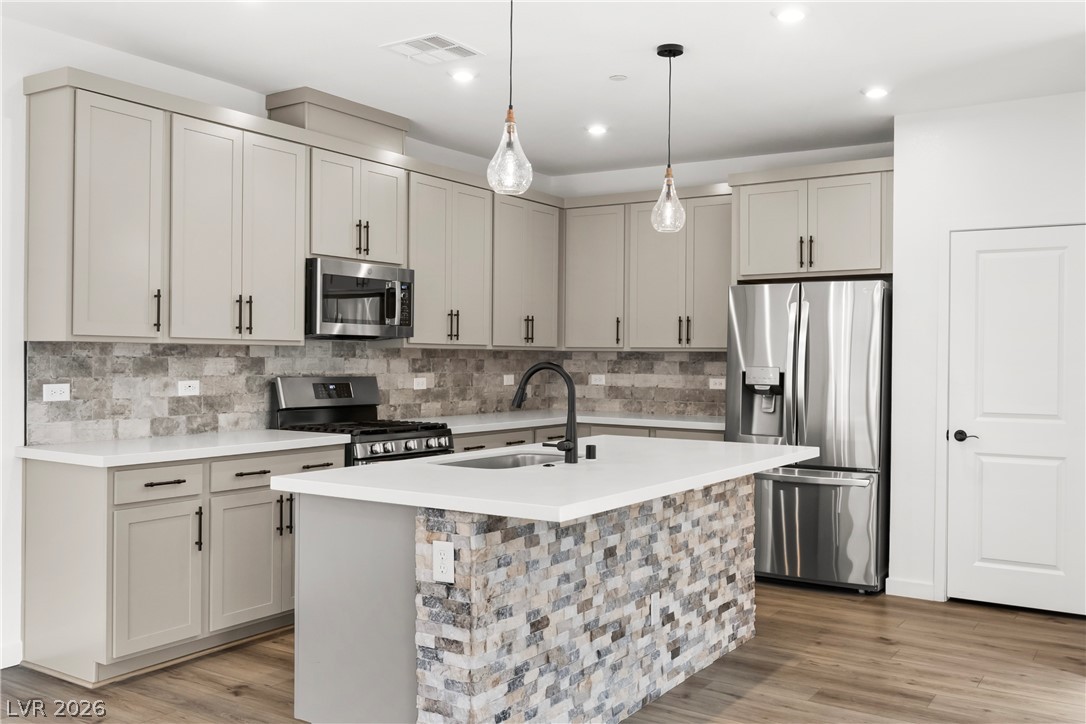 633 Infinity Rdg Street Las Vegas, NV 89138 - Photo 5 of 36 Kitchen with stainless steel appliances, a center island with sink, light wood-style floors, pendant lighting, and decorative backsplash
