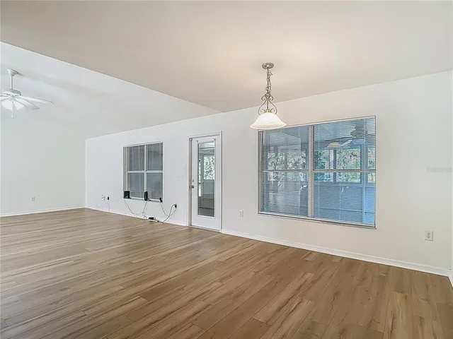 an empty room with wooden floor chandelier fan and windows