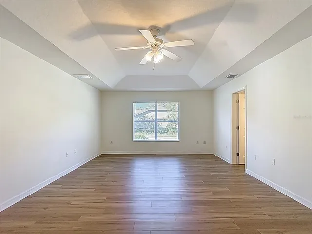 an empty room with wooden floor fan and windows